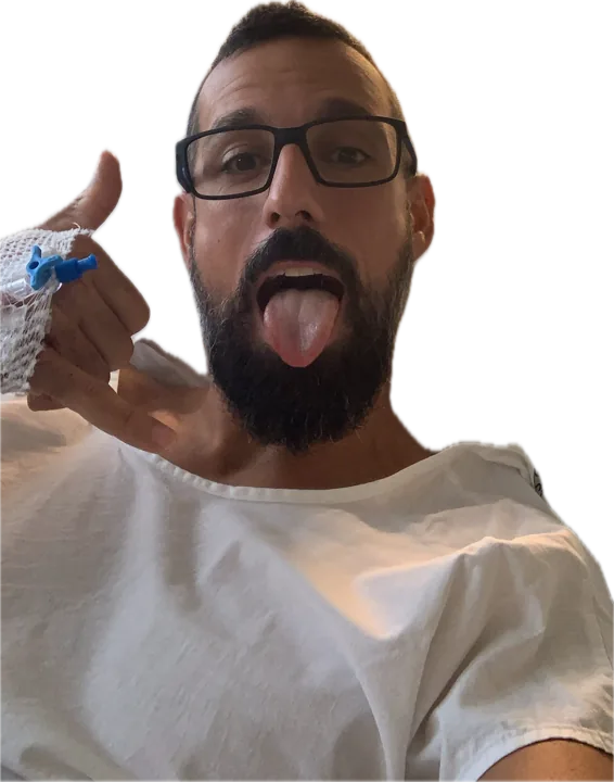 Roger en la cama del hospital, con la vía puesta, sacando la lengua